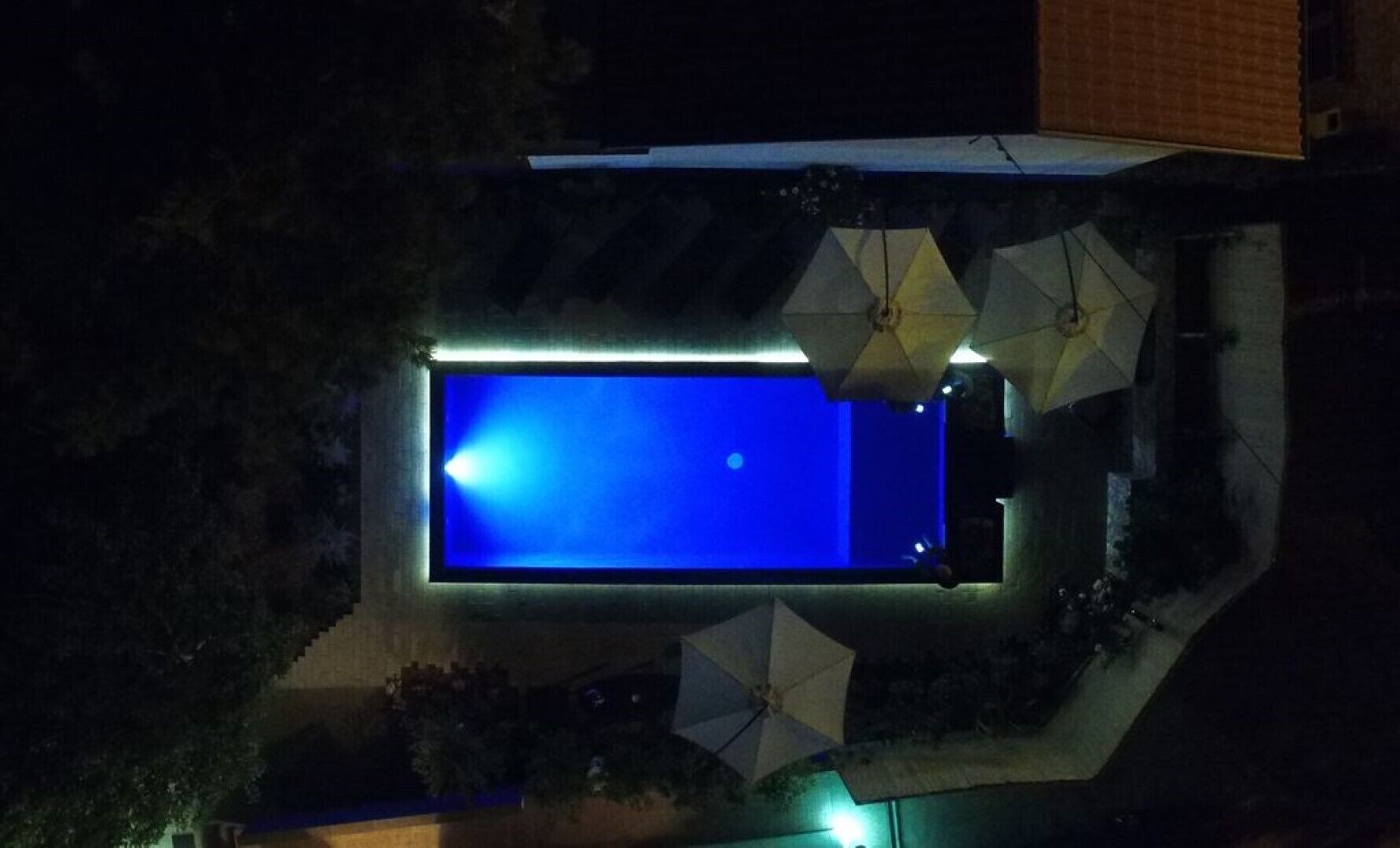 Vue aérienne d’une piscine rectangulaire à l’eau bleue, entourée de parasols et d’une petite zone aménagée en terrasse.