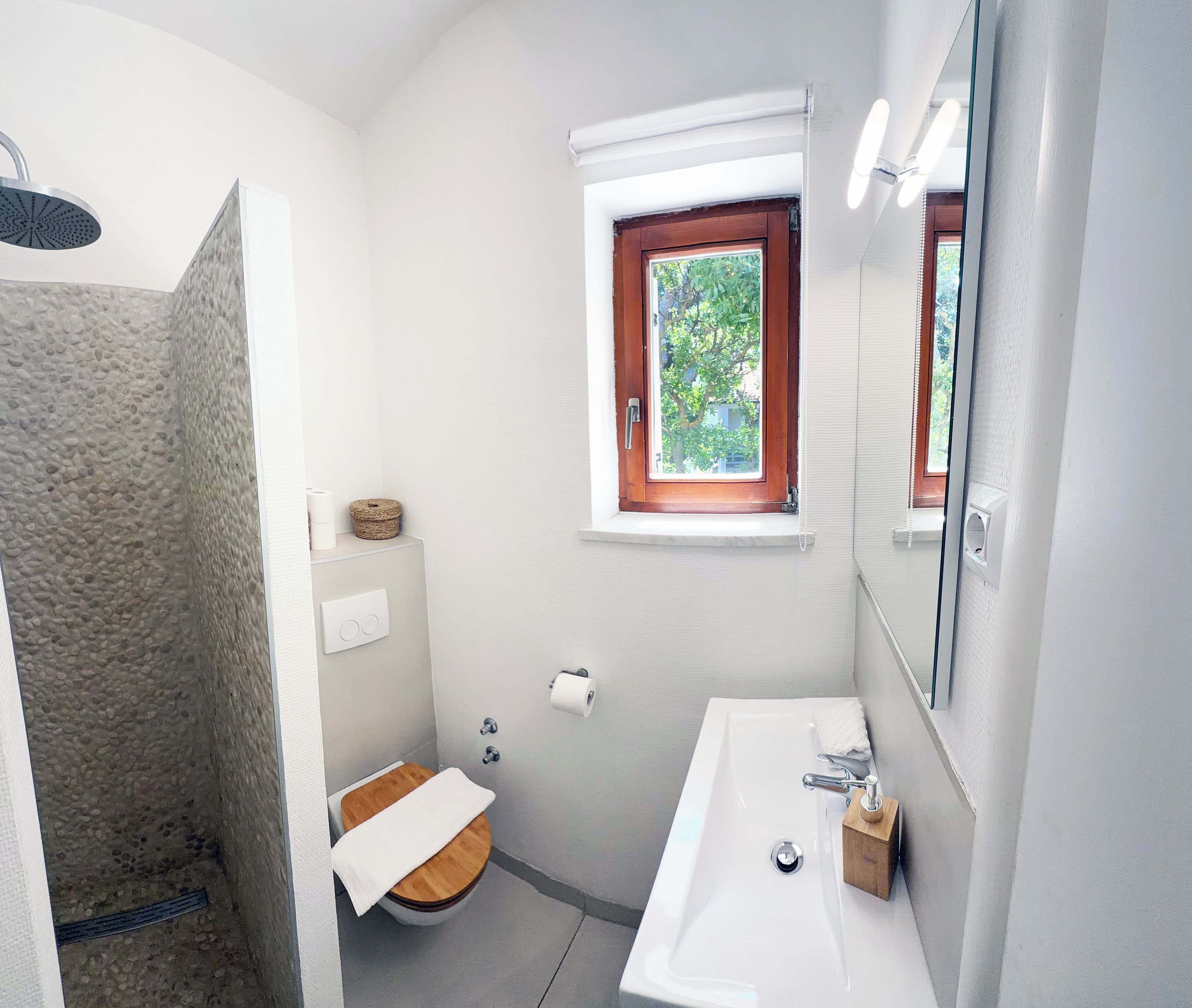 A bathroom with a shower, toilet, sink, and a window with a view of greenery.