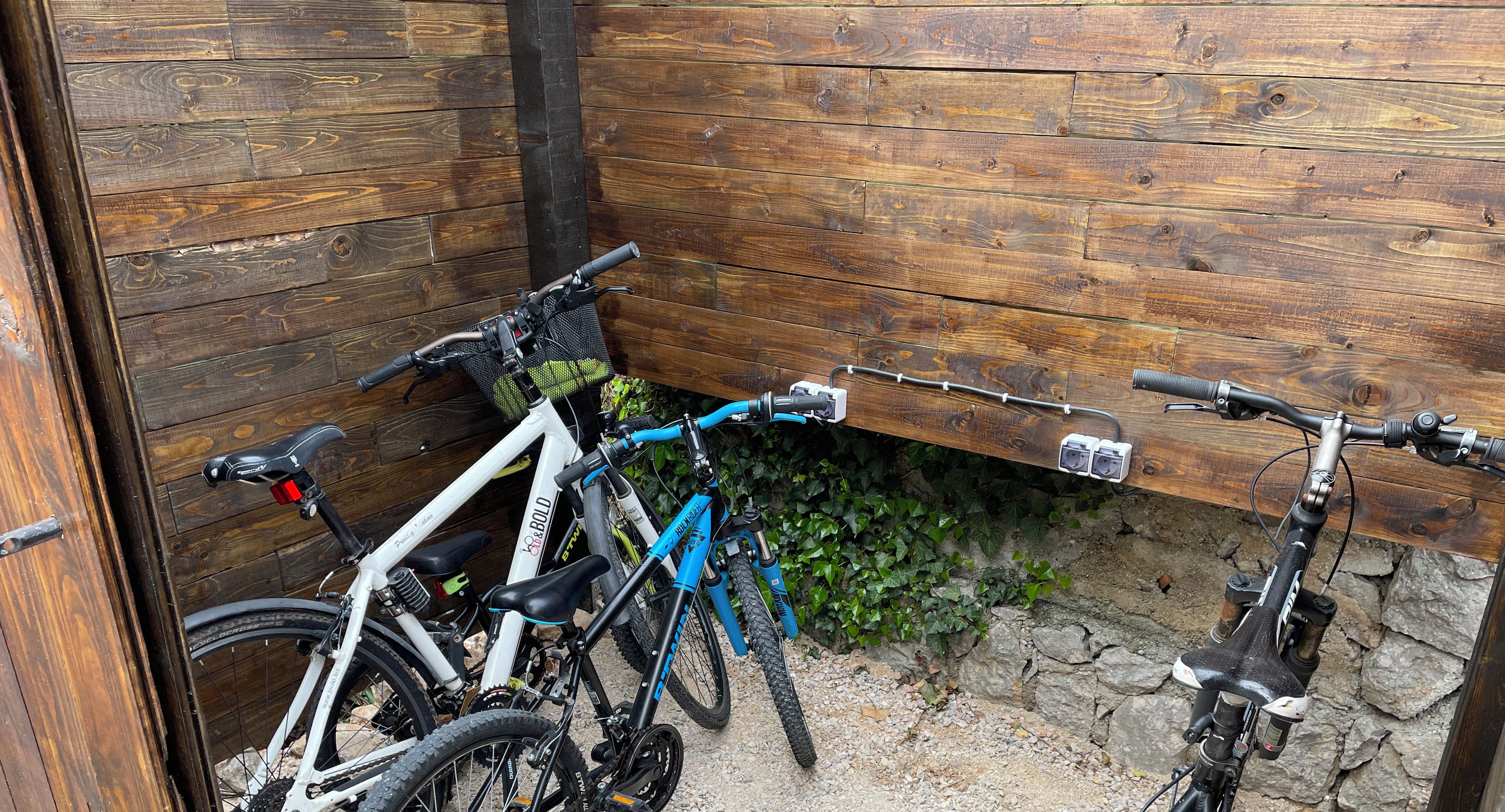 Een fietsenstalling met houten wanden en een grindvloer, geschikt voor 4 tot 5 fietsen.