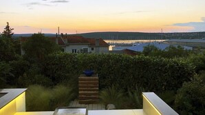 Uma área de estar moderna ao ar livre com vista para uma marina e colinas ao longe.
