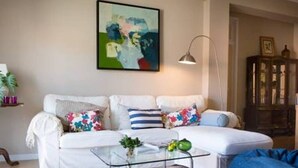 A living room with a white sofa, a glass coffee table, and a colorful abstract painting on the wall. - Peaceful Top Floor Apt W Balconies-Cambridge RIGHT (AC) (Funchal)