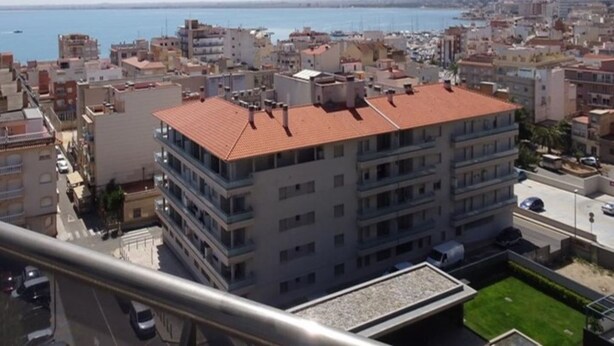 A multi-story building with a red-tiled roof, surrounded by other buildings and a body of water in the background. - Marisol apartment - sea view - 100m from the sea - swimming pool - airco (L'Ampolla)