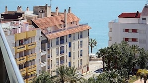 Un edificio costero con varios balcones, techo de tejas rojas y vista al mar.