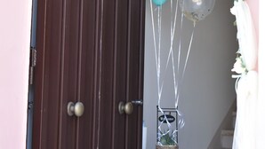 Una puerta de madera adornada con globos azul turquesa y blancos, un cartel de bienvenida y un adorno decorativo.