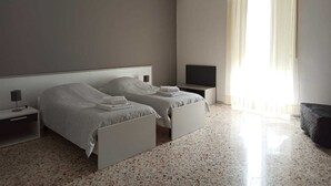 Un dormitorio moderno con dos camas, un televisor de pantalla plana y un ventanal con cortinas translúcidas.