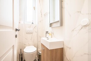 A modern bathroom with a marble wall, a wooden cabinet, a white sink, and a toilet. - halu! Stylish & Bright Centre Home (Thessaloniki)