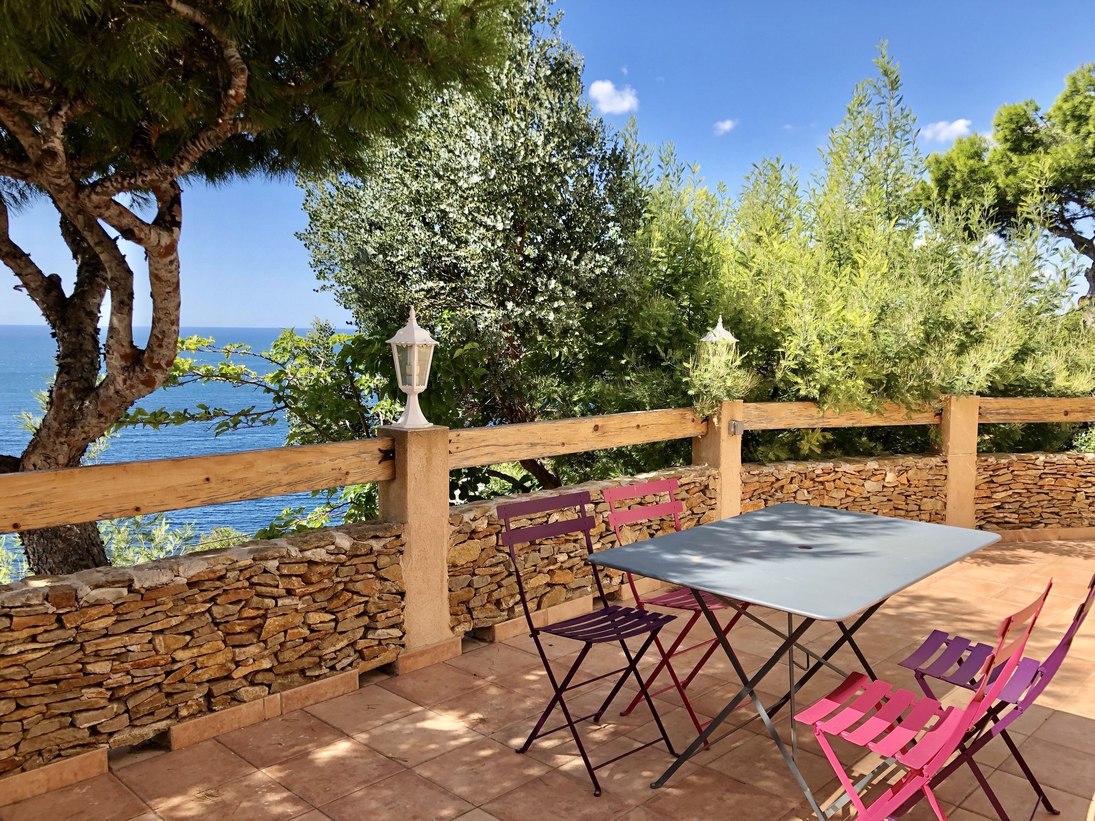 An outdoor seating area with a stone wall, wooden fence, and a view of the sea.