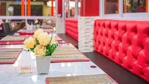L’intérieur d’un restaurant présente un banc rembourré de coussins rouges, une table ornée d’un vase de roses jaunes et un chemin de table à motifs.