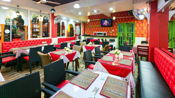 Un restaurant avec des banquettes rouges, des tables recouvertes de nappes blanches et des ventilateurs de plafond.
