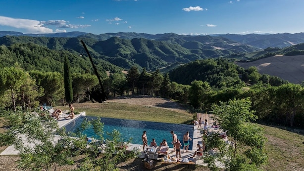 Area piscina con vista sulle montagne, circondata da alberi e persone che si rilassano.