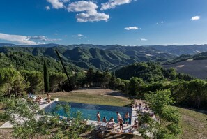 A pool area with a view of mountains, surrounded by trees and people relaxing. - Il Pavone Errante (Mercato Saraceno)