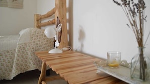 Una scrivania in legno con una lampada, un vaso di vetro con piante essiccate e un letto con biancheria da letto a motivi floreali.