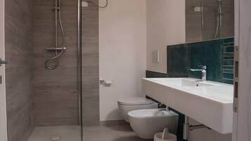 Ein modernes Badezimmer mit einer gläsernen Duschkabine, einem weißen Waschbecken und einer Toilette.