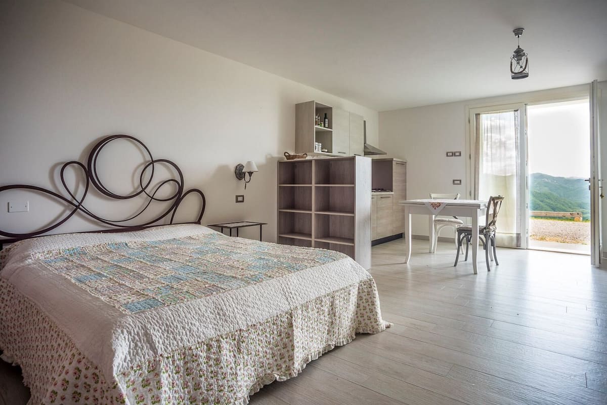 Quarto com cama, escrivaninha e vista para o exterior.