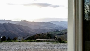 Paesaggio montuoso visibile da una finestra, con un vialetto sterrato e una panchina in primo piano.
