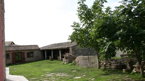 A stone building with a tiled roof, a grassy yard, and a wooden fence. - Sa Domu De Sa Contissa (Selegas)