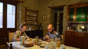 A dining table set with plates, cups, and a pitcher of water in a stone-walled room with wooden cabinets and a window. - Sa Domu De Sa Contissa (Selegas)