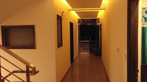 A narrow hallway with a staircase on the left, a door with a green curtain on the right, and a light fixture above the stairs. - Hotel Aerocity Golden (New Delhi)