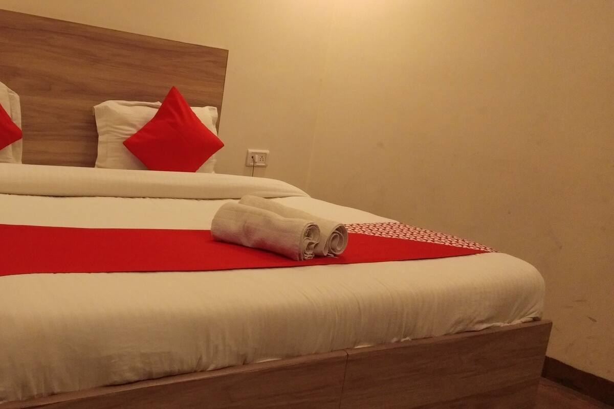 A neatly made bed with white and red bedding, a wooden headboard, and a red throw blanket.
