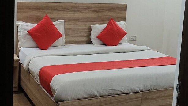 A neatly made bed with a wooden headboard, white bedding, and red accents. - Hotel Aerocity Golden (New Delhi)