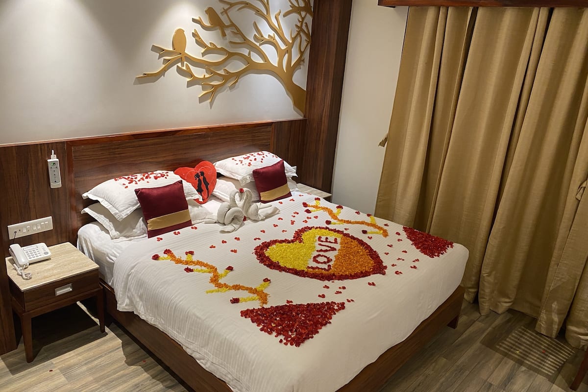 A hotel room with a neatly made bed, a wooden headboard, a bedside table with a phone, and a wall-mounted decorative tree.