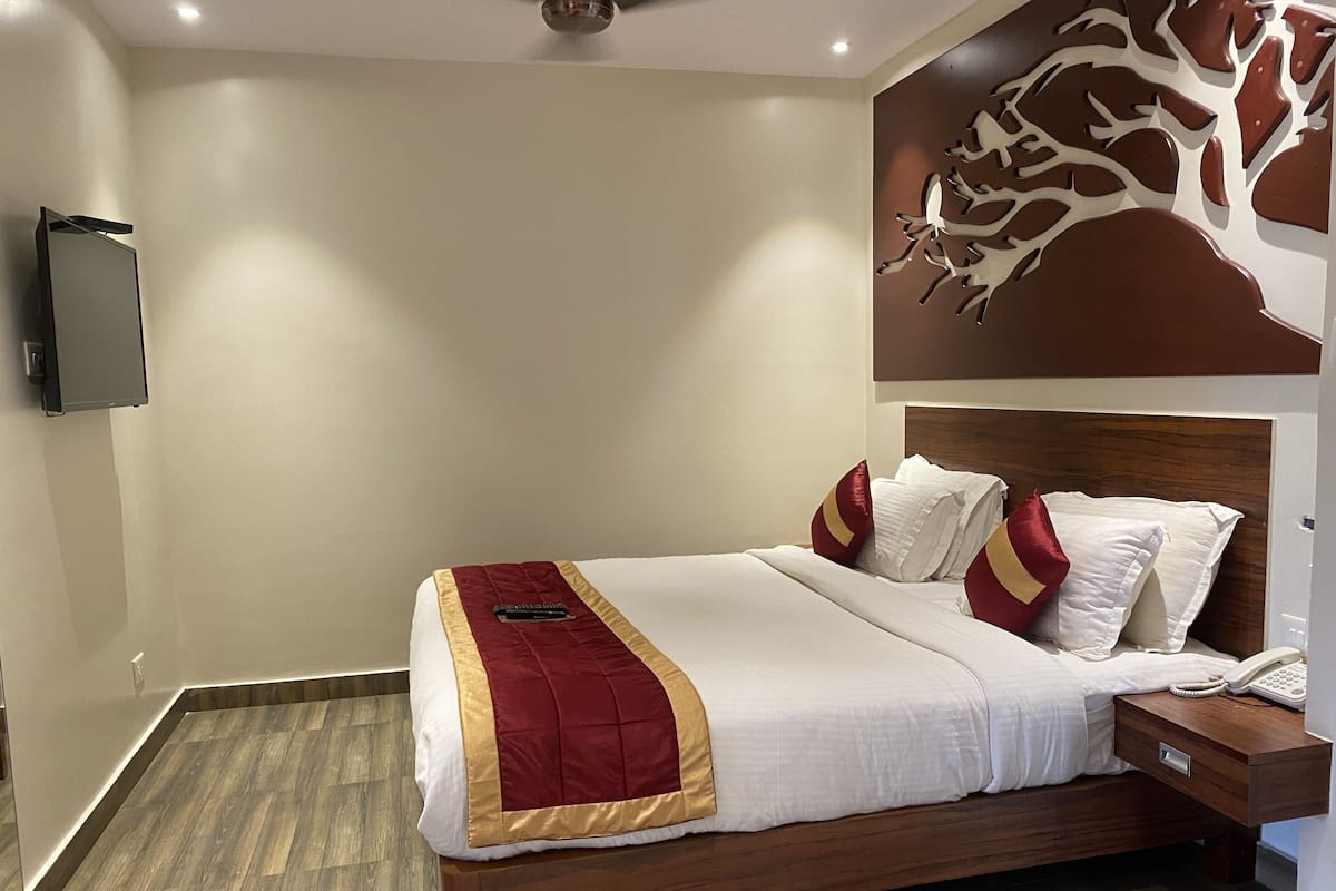 A neatly made bed with a red and gold bedspread, white pillows, and a wooden nightstand with a telephone.