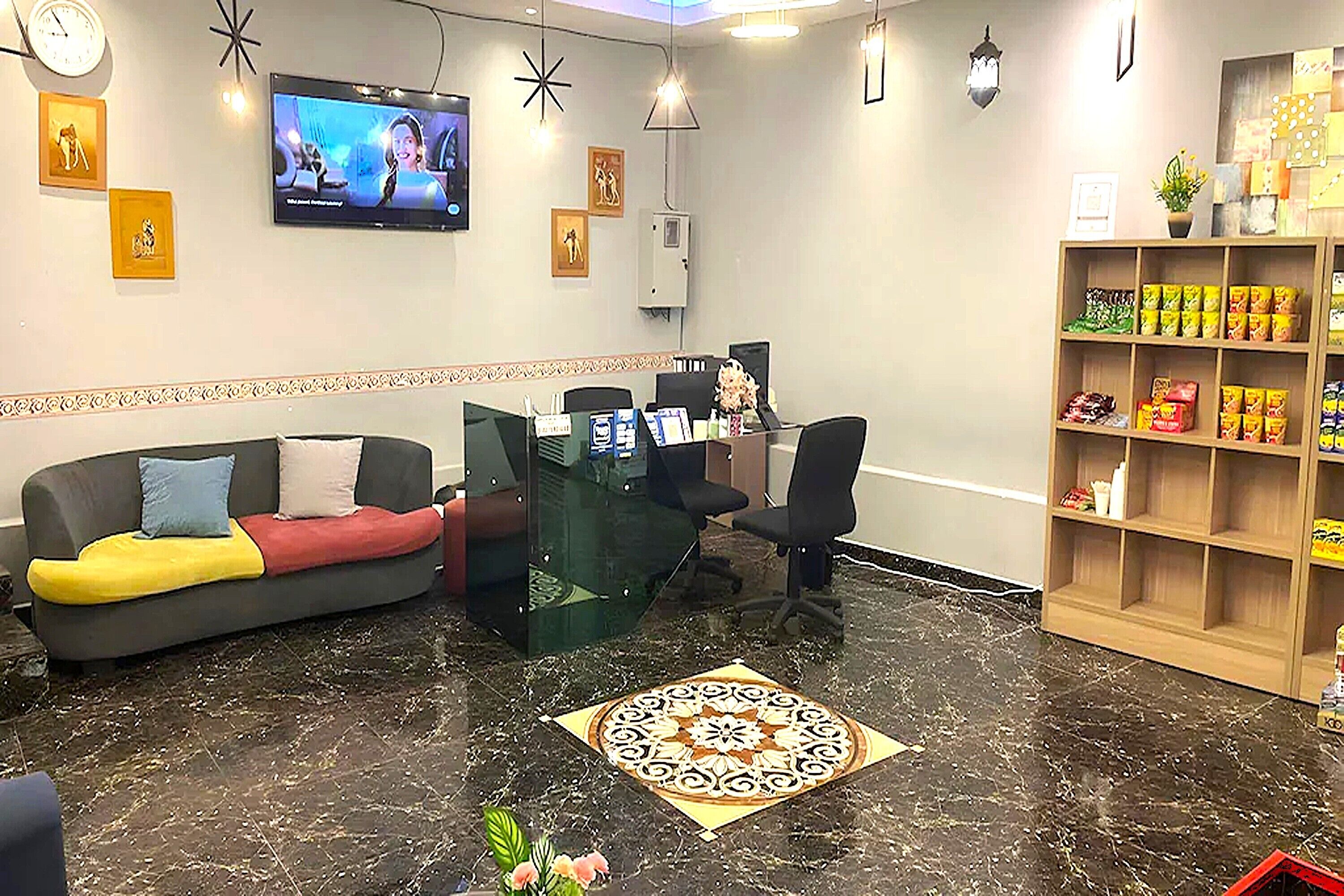 Et receptionsområde med sofa, receptionsskrank, fjernsyn og en reol med snacks.