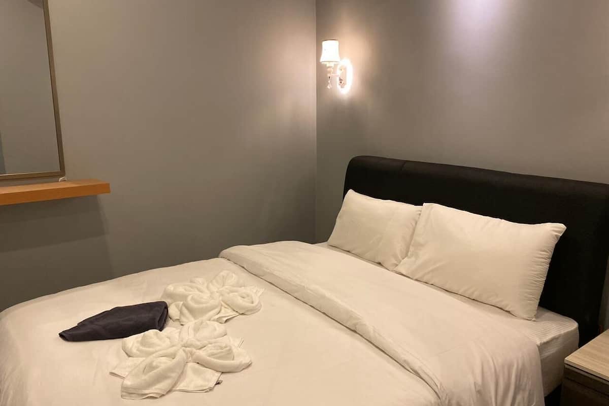 Una cama bien hecha con sábanas blancas y un cabecero oscuro, una mesita de noche y un aplique de pared.