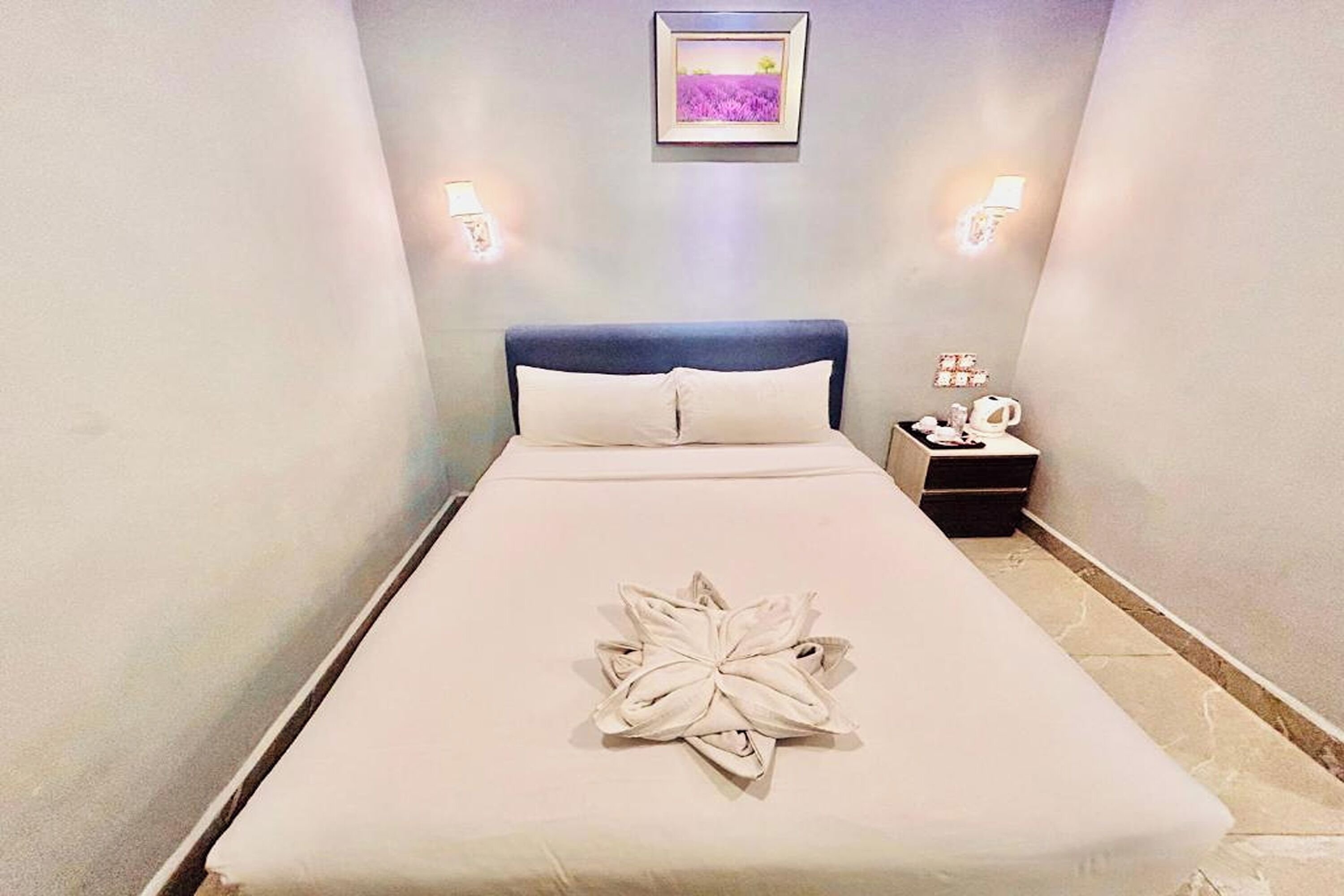 A neatly made bed with a towel art centerpiece, a nightstand with a lamp, and a framed picture on the wall.
