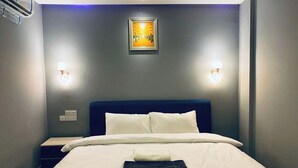 Ein ordentlich bezogenes Bett mit weißen Leinen und einem gefalteten Handtuch, ein dunkelblaues Kopfteil und zwei Wandleuchten.