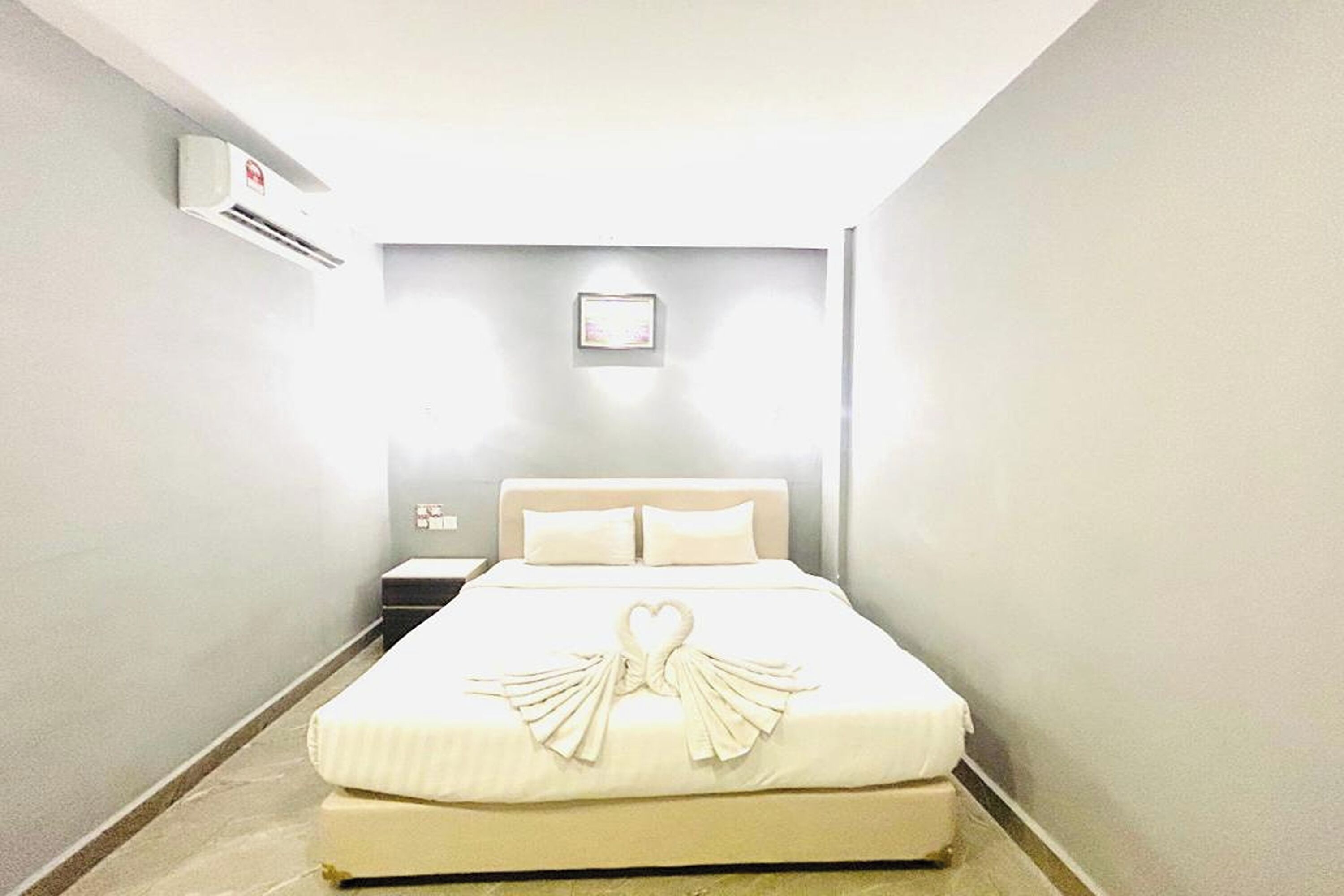 Une chambre d’hôtel avec un lit, une table de chevet et un climatiseur fixé au mur.