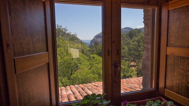 A wooden-framed window with a view of a terracotta-tiled roof and lush greenery. - Agriturismo Quercia Antica (Terranova di Pollino)