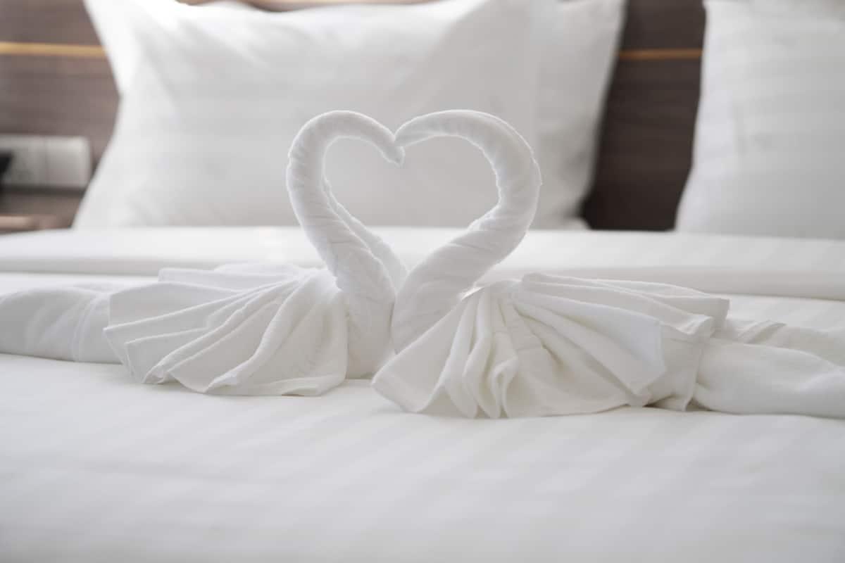 A bed with white linens and two towels arranged in the shape of a heart.