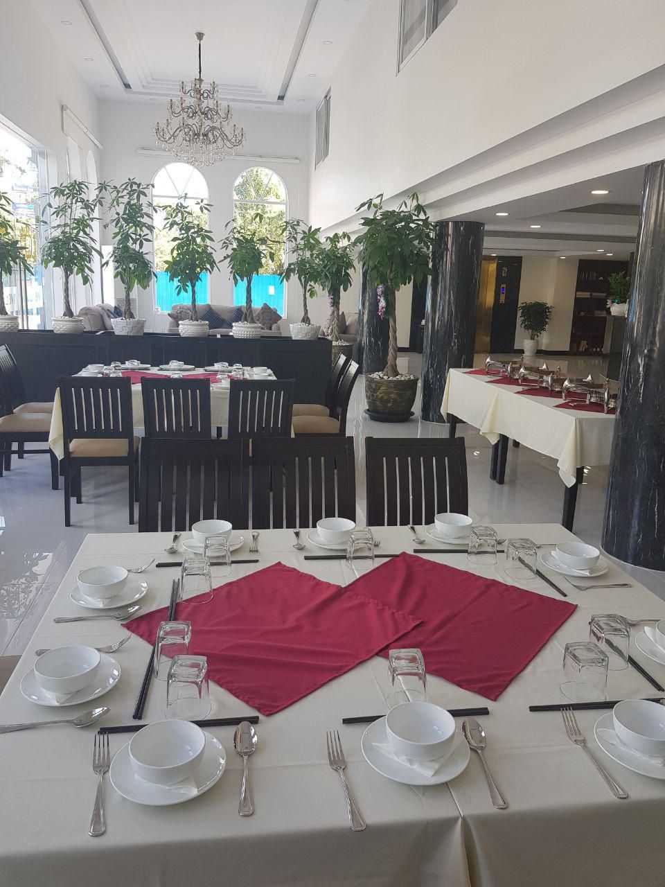 A dining area with tables set for service, large windows, and potted plants.