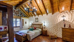 Quarto rústico com teto de madeira, parede de pedra e cama com cabeceira de madeira.