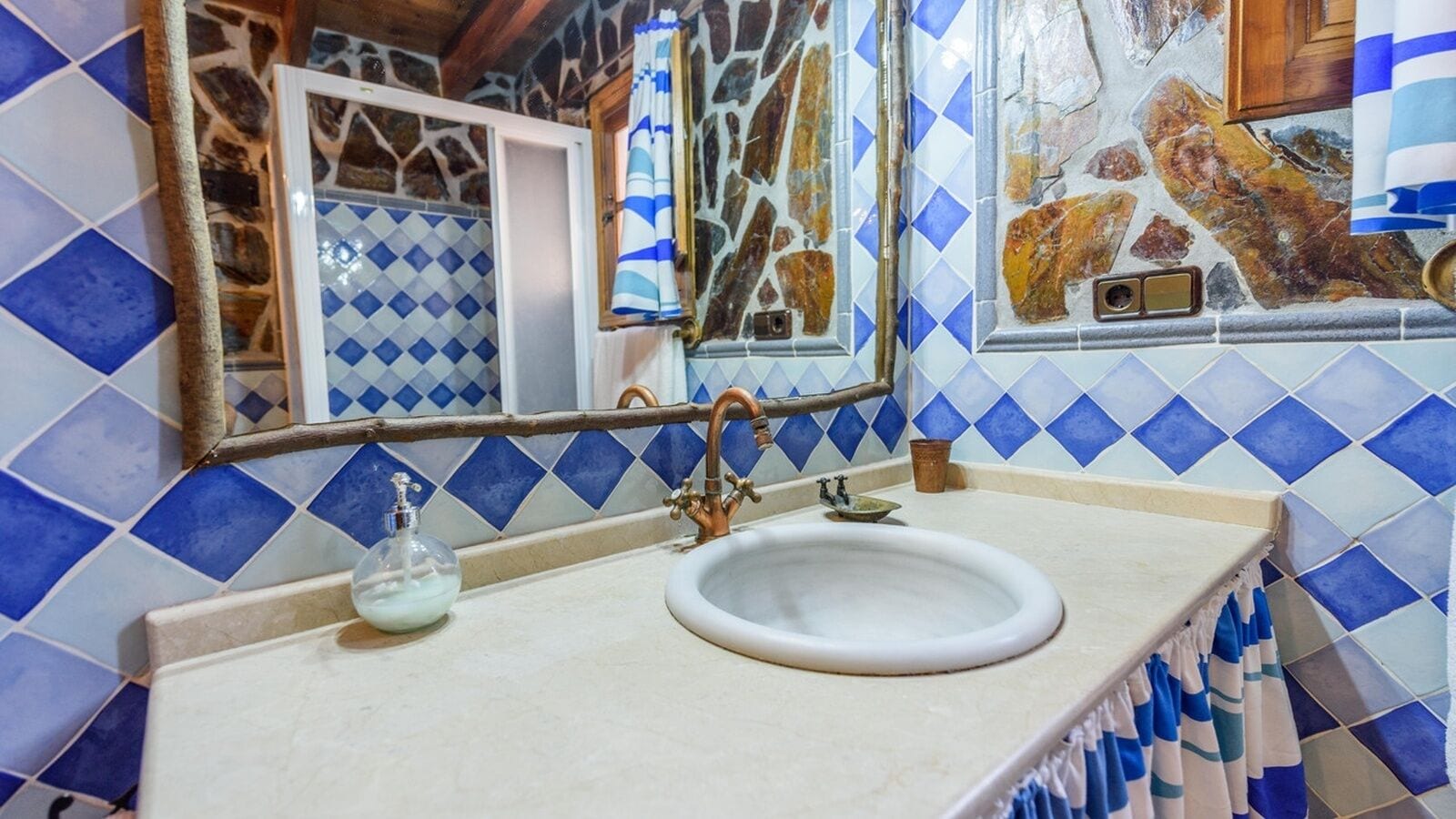 Un baño con un lavamanos blanco, mosaicos azules y blancos y un espejo con marco de madera.
