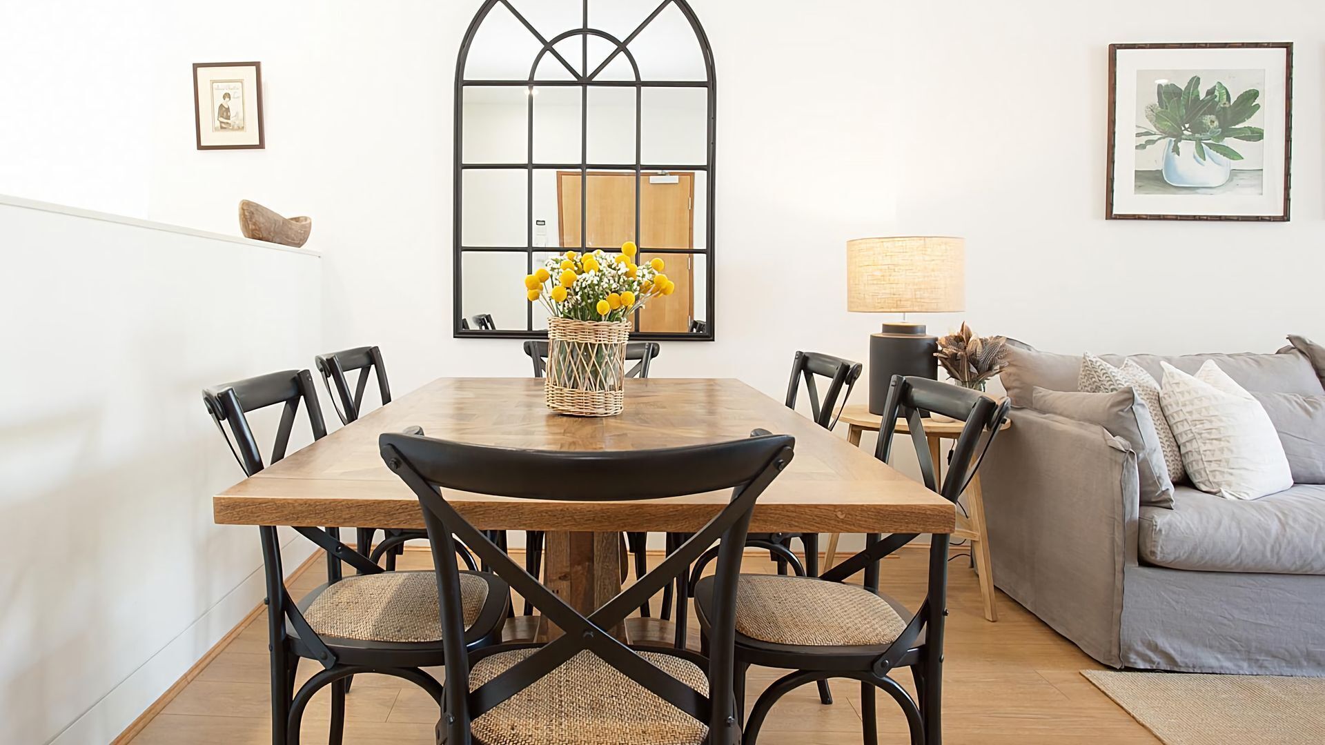 A dining area with a wooden table, black chairs, and a woven basket with yellow flowers.