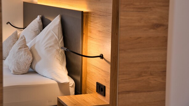 A bed with a wooden headboard, a bedside table, and a wall-mounted light fixture. - Landgasthof Hirschen (Hohentengen am Hochrhein)
