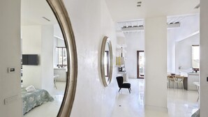 A spacious hotel room with a large mirror, a bed with a floral bedspread, a small table with chairs, and a kitchenette area.