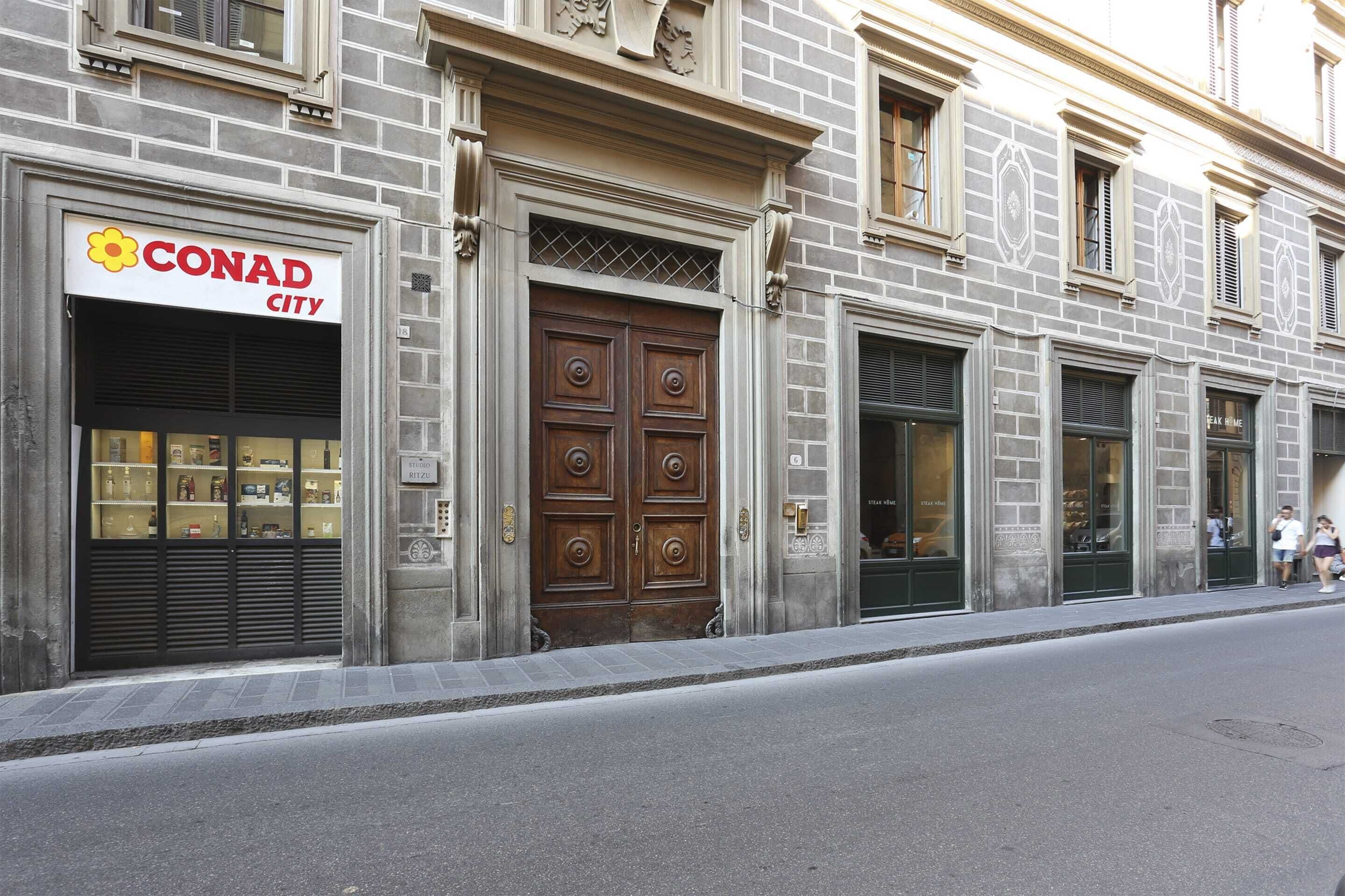A building with a CONAD CITY sign, large wooden doors, and a brick facade.