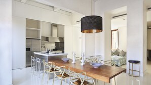 A modern kitchen with a wooden dining table, white chairs, and a black pendant light.