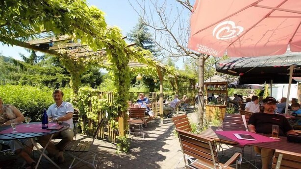 An outdoor café with tables and chairs, surrounded by greenery and a pergola. - Hotel Saalestrand (Unterwellenborn)