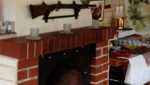 A fireplace with a brick surround, a mantel with various items, and a table with a white tablecloth to the right. - Hotel Saalestrand (Unterwellenborn)