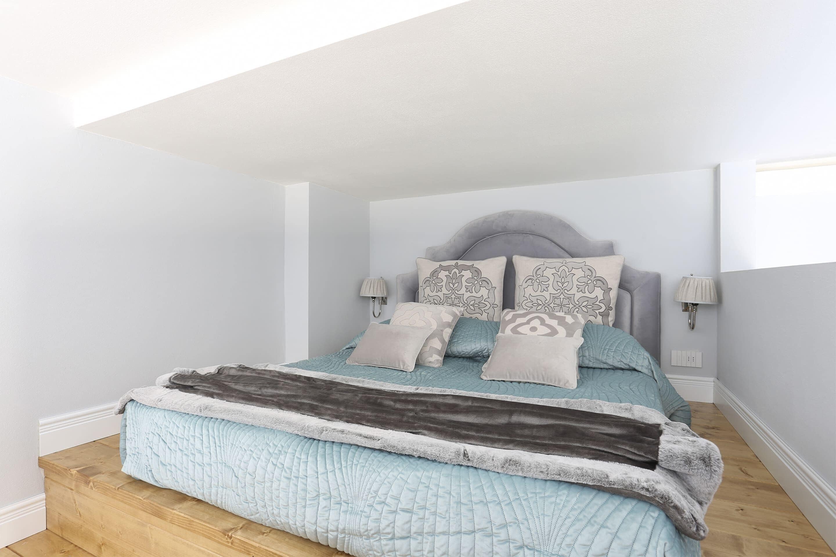 A bedroom with a bed, headboard, bedside lamps, and a window.