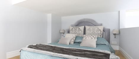 A bedroom with a bed, headboard, bedside lamps, and a window.