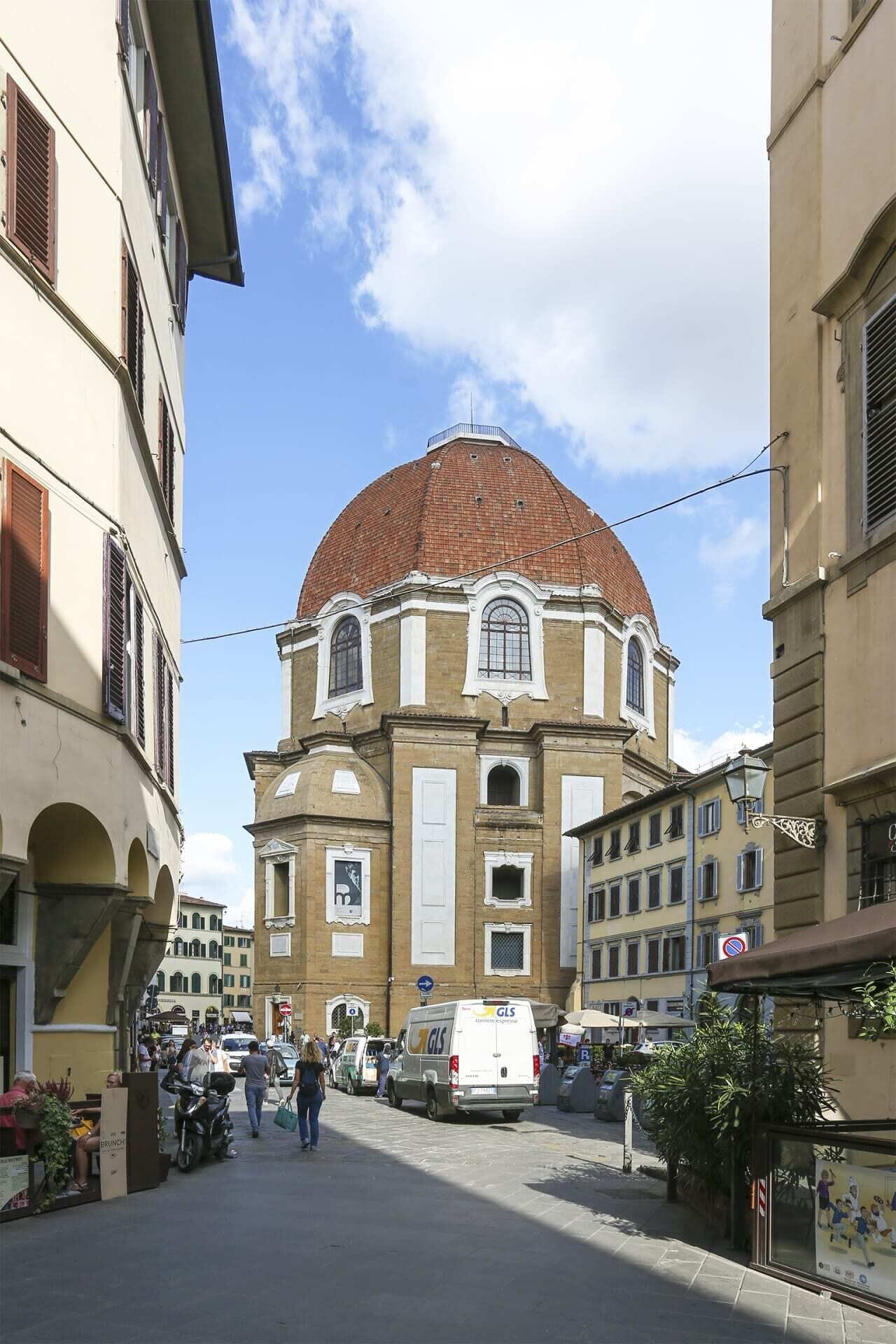 Ein historisches Gebäude mit Kuppel und Bogenfenstern, umgeben von einer belebten Straße mit Fußgängern und Fahrzeugen.