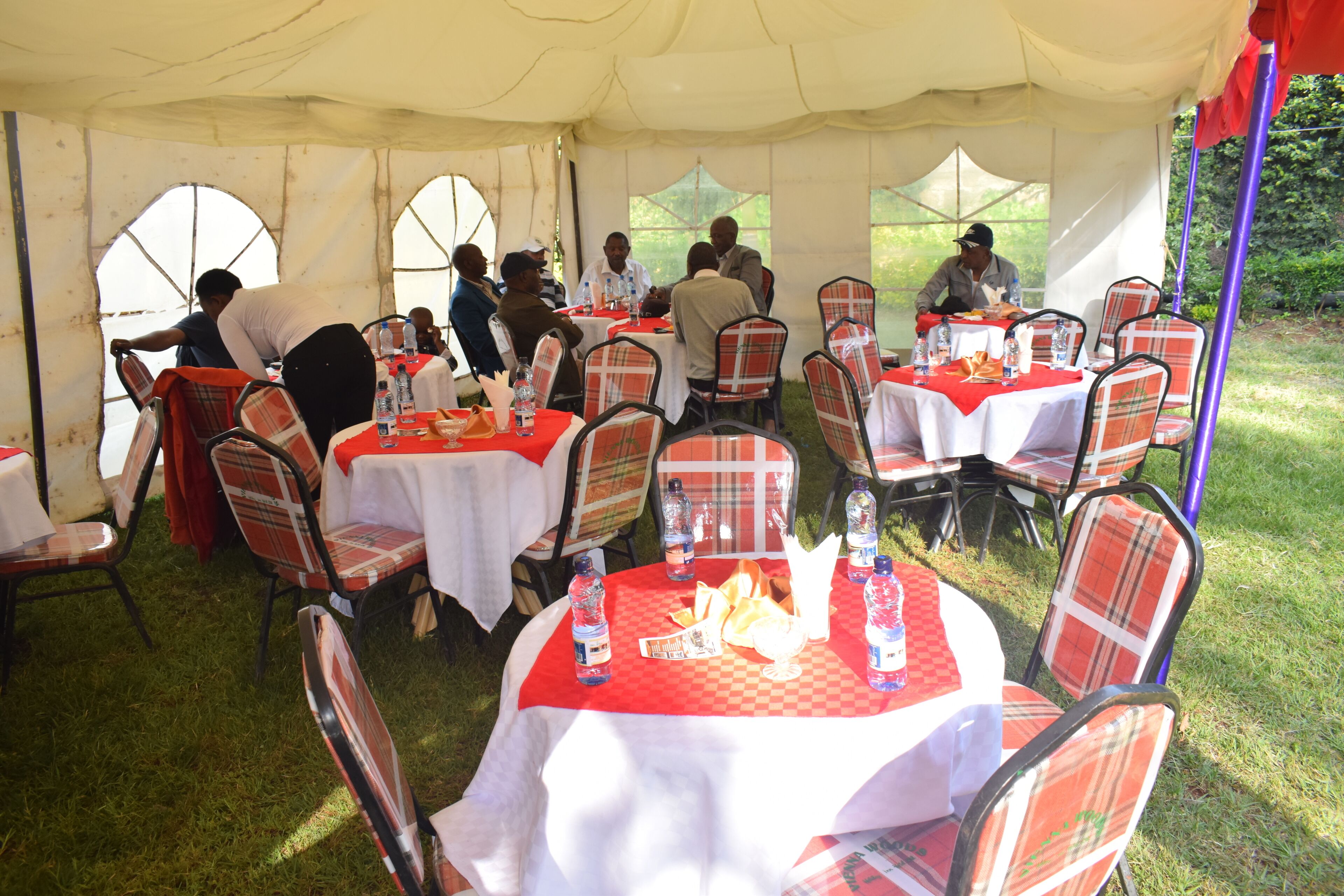 A tented dining area with round tables covered in white tablecloths and plaid chairs.