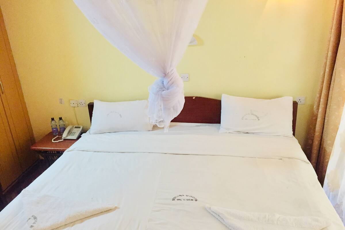 A hotel room with a bed, white linens, a bedside phone, and a nightstand with bottled water.