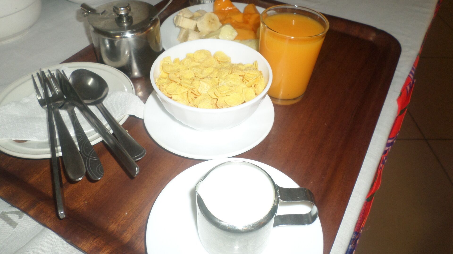 A breakfast tray with cereal, fruit, a glass of orange juice, and cutlery.