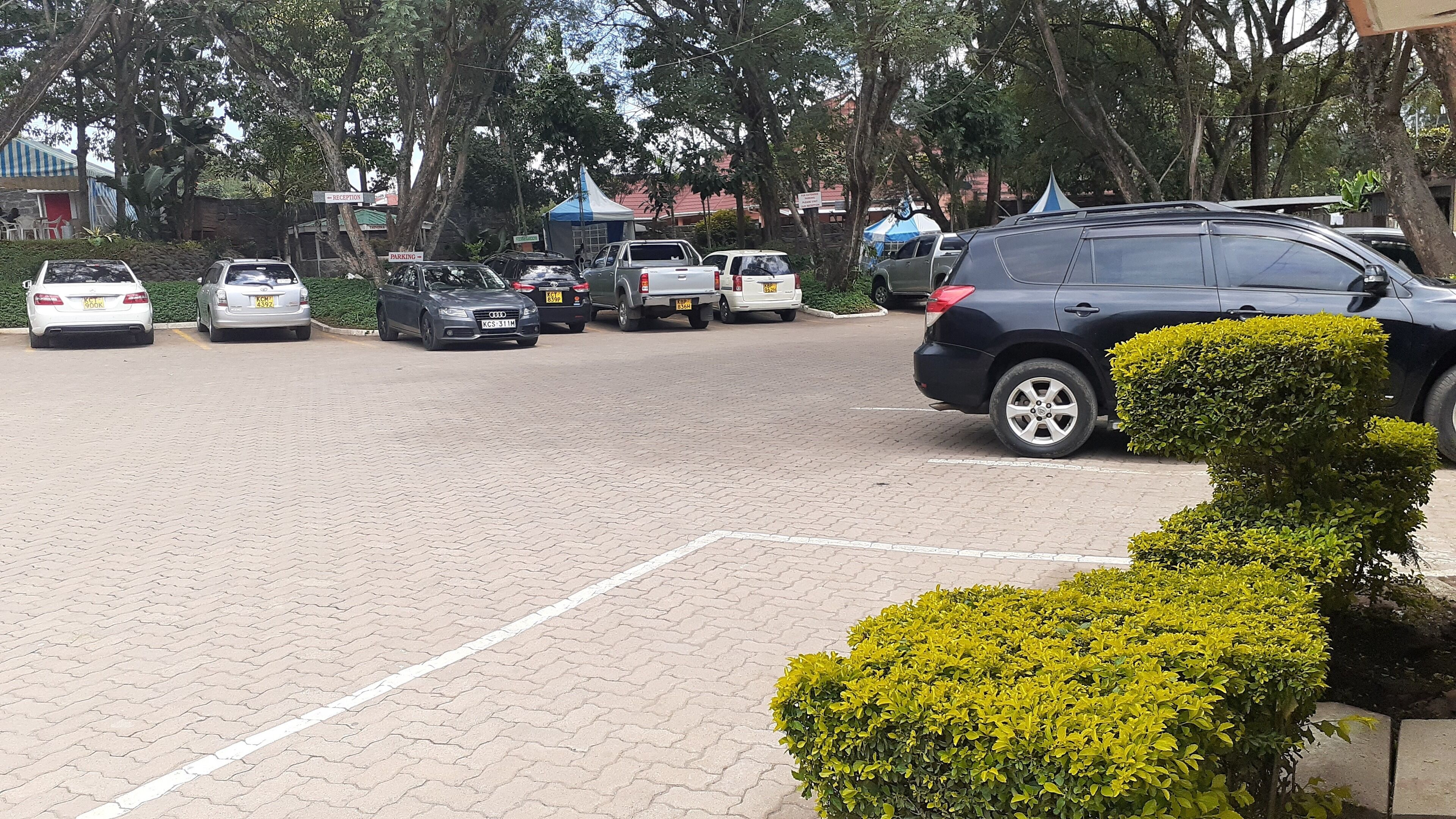 A parking area with multiple cars and a reception tent in the background.